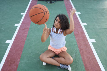 A little girl sitting down spins a basket ball - CAVF90953