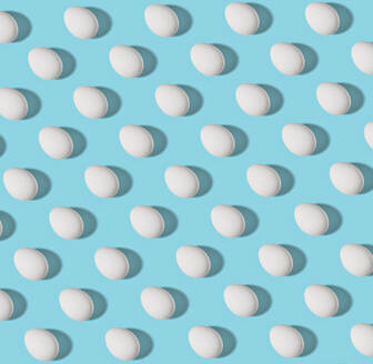 Pattern of white chicken eggs against blue background - RAMF00096