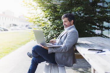 Businessman using laptop while leaning on table - DGOF01741