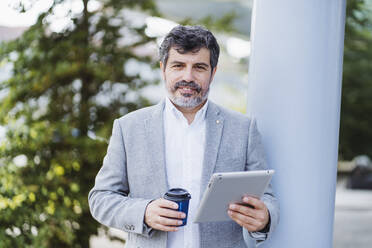 Geschäftsmann mit digitalem Tablet und Einweg-Kaffeebecher an der Säule - DGOF01744