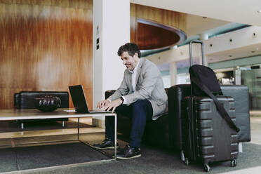 Älterer Geschäftsmann, der einen Laptop benutzt, während er in der Hotellobby sitzt - DGOF01752