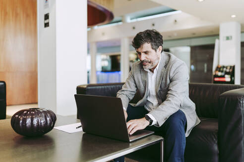 Male entrepreneur using laptop while sitting at lobby in hotel - DGOF01753