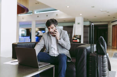 Geschäftsmann, der in der Hotellobby mit einem Laptop telefoniert - DGOF01755