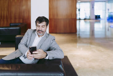 Businessman using mobile phone in hotel lobby - DGOF01759