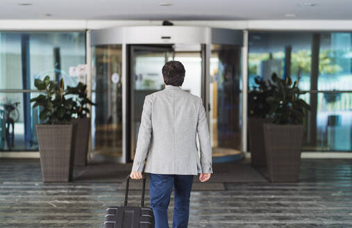 Businessman pulling wheeled luggage while leaving hotel - DGOF01762