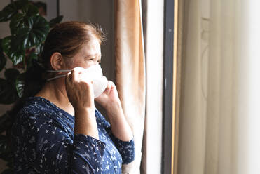 Frau im Haus während der Quarantäne mit Blick durch das Fenster nach draußen - CAVF90976