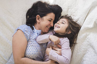 Laughing mom and 6 yr old daughter snuggling in bed - CAVF91062