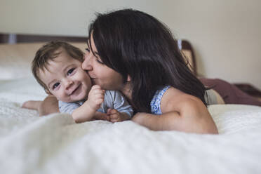 Liebevolle Mutter küsst süßes lächelndes Baby im Liegen auf dem Bett - CAVF91063