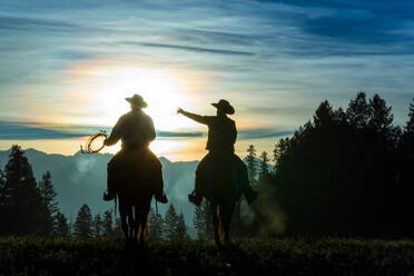 Zwei Cowboys reiten über Grasland mit Bergen im Hintergrund, früher Morgen, Britisch-Kolumbien, Kanada. - MINF15357