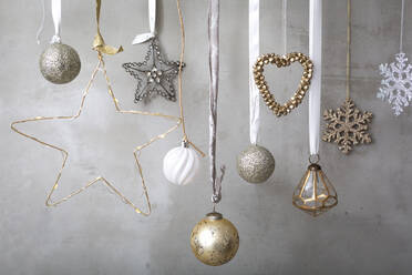 Christmas decorations, close up of silver, white and golden Christmas baubles on ribbons on grey background. - MINF15364