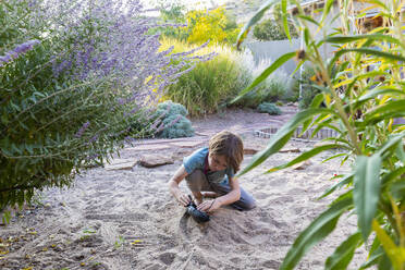 7 year old boy playing in sandy garden with his toy ship. - MINF15391