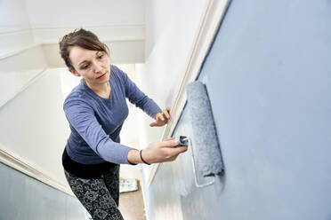 Frau benutzt Farbroller zum Streichen einer Treppe - MINF15409