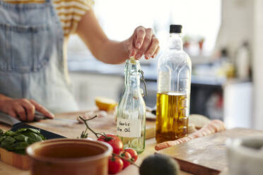 Frau legt Knoblauch in eine Flasche Olivenöl in der Küche - MINF15412