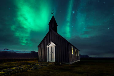 Prächtige Kulisse einer Holzkirche auf einer Wiese vor dem Hintergrund eines Himmels mit Polarlichterscheinungen in Island bei Nacht - ADSF17745