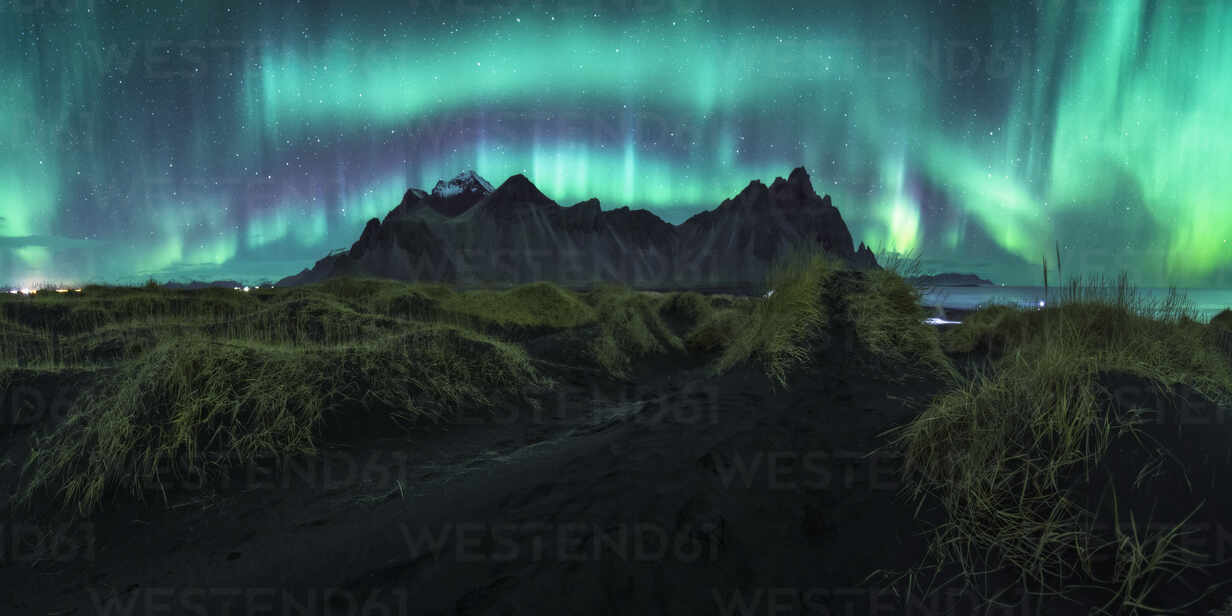Malerische Landschaft mit Polarlicht über felsigem Gelände mit Bergen bei  dunkler Nacht in Island in langer Belichtung, lizenzfreies Stockfoto