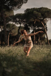 Tranquil female ballet dancer balancing barefoot on meadow in park in Iceland while performing with closed eyes and outstretched arms - ADSF17765