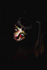 Gruselige Frau mit bemaltem Gesicht und Kontaktlinsen, die nachts an Halloween aus einem dunklen Raum herausschaut - ADSF17786