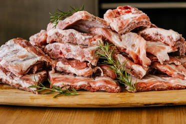 Heap of uncooked meat ribs with fat and aromatic rosemary sprigs on wooden table - ADSF17792