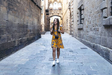 Mid adult woman smiling while walking on footpath at Gothic Quarter, Barcelona, Catalonia, Spain - JSRF01187