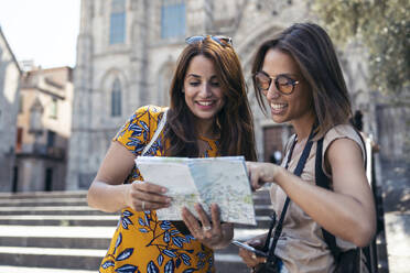 Ein lächelnder Freund hält eine Landkarte in der Hand, während er am Platz der Kathedrale von Barcelona in Barcelona, Katalonien, Spanien steht - JSRF01200