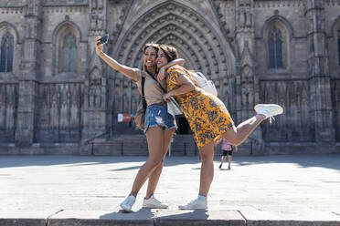 Frau, die ihren Freund umarmt, während sie ein Selfie mit ihrem Mobiltelefon auf dem Platz der Kathedrale von Barcelona in Barcelona, Katalonien, Spanien, macht - JSRF01203