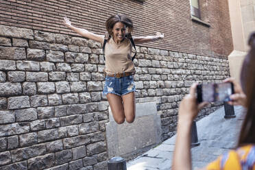 Ein Freund fotografiert eine Frau, die im Gotischen Viertel in Barcelona, Katalonien, Spanien, gegen die Wand springt - JSRF01210