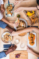 Top view crop multiethnic friends gathering at table in modern restaurant and having tasty dinner including meat balls spring rolls and sandwiches - ADSF17881