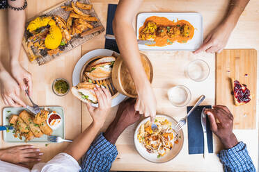 Top view crop multiethnic friends gathering at table in modern restaurant and having tasty dinner including meat balls spring rolls and sandwiches - ADSF17882