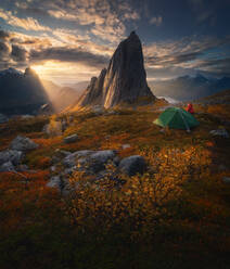 Unrecognizable female tourist camping and admiring highland while standing on mountain under sky at sunset - ADSF17892