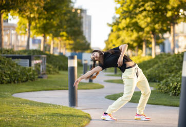 Side view of young active stylish female in trendy outfit dancing on pathway in city park on sunny day - ADSF17943