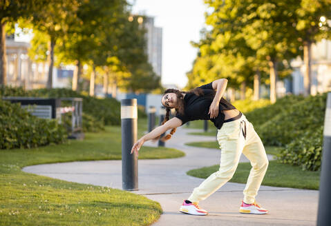 Seitenansicht der jungen aktiven stilvolle Frau in trendigen Outfit tanzen auf dem Weg in der Stadt Park am sonnigen Tag - ADSF17943