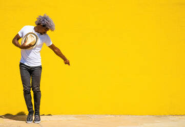 Black man with afro hair and hat dancing on a yellow background. Dancing with a hat. - ADSF17977