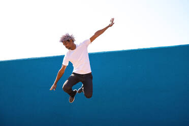 Black and afro man dressed in white jumping on a blue wall. Parkour concept. - ADSF17979