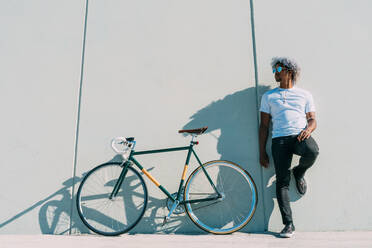 Schwarzer Radfahrer lehnt an einer grauen Wand neben seinem Stadtrad. Schwarzer Radfahrer Konzept. Afro-Radfahrer. - ADSF17981