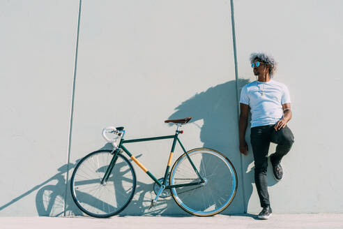 Schwarzer Radfahrer lehnt an einer grauen Wand neben seinem Stadtrad. Schwarzer Radfahrer Konzept. Afro-Radfahrer. - ADSF17981