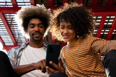 Von unten der lächelnden diverse Paar von Freunden mit Afro-Frisur beobachten Handy unter der Decke im Hintergrund beleuchtet - ADSF17992