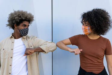 Anonymer junger afroamerikanischer Mann und Frau mit lockigen Haaren in Freizeitkleidung und Schutzmasken, die sich mit den Ellbogen an einer weißen Wand abstützen - ADSF18016