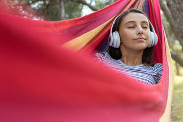 Friedliche Frau mit Kopfhörern, die in der Hängematte liegt und mit geschlossenen Augen ruhige Musik genießt - ADSF18031