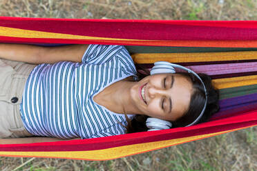 Peaceful female in headphones lying in hammock and enjoying calm music with closed eyes - ADSF18032