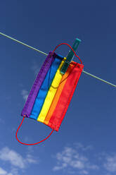 Schutzmaske mit Bild der LGBT-Regenbogenflagge, die mit einer Wäscheklammer an einem sonnigen Tag im Hinterhof befestigt wird - ADSF18040