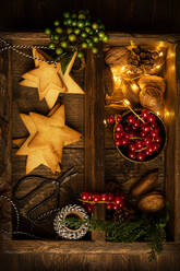 Draufsicht auf leckere Plätzchen in Form von Sternen und roten Beeren, die mit beleuchteter Girlande und Nüssen auf einem Holztisch in einem dunklen Raum für eine Weihnachtsfeier angeordnet sind - ADSF18048