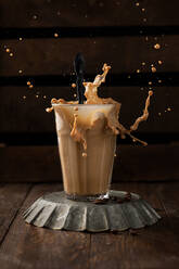 Glass of aromatic coffee with milk splashing above wooden table in coffee shop - ADSF18054