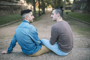 Homosexuelles Paar, das sich auf einem Fußweg in einem öffentlichen Park sitzt und sich ansieht - GRCF00510