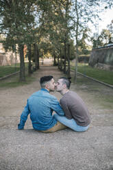 Zärtliches schwules Paar küsst sich auf dem Fußweg in einem öffentlichen Park - GRCF00511