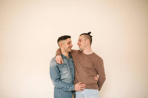 Glückliches schwules Paar mit Arm um stehend gegen beige Hintergrund - GRCF00523