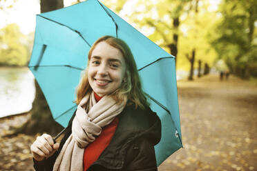 Teenager-Mädchen mit Regenschirm lächelnd, während auf der Straße im Park stehen - JATF01267