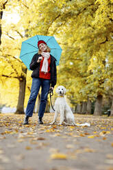 Teenager-Mädchen hält Regenschirm, während sie mit ihrem Haustier auf der Straße im Park steht - JATF01269