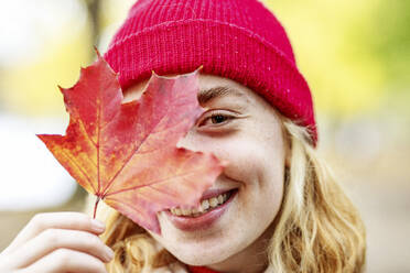 Teenage girl wearing hat covering face with leaf outdoors - JATF01276