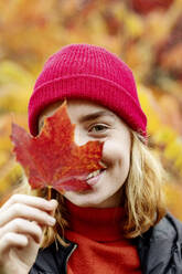 Teenage girl wearing knit hat holding maple leaf outdoor - JATF01279