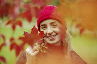 Lächelndes Teenager-Mädchen, das ein Ahornblatt hält, während es im Freien steht - JATF01280